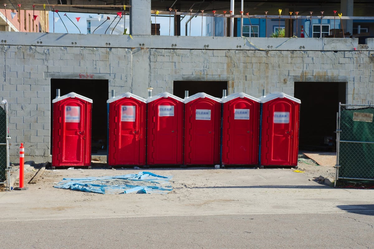 Collection of bright red portable restrooms placed in front of a concrete wall on an active construction site