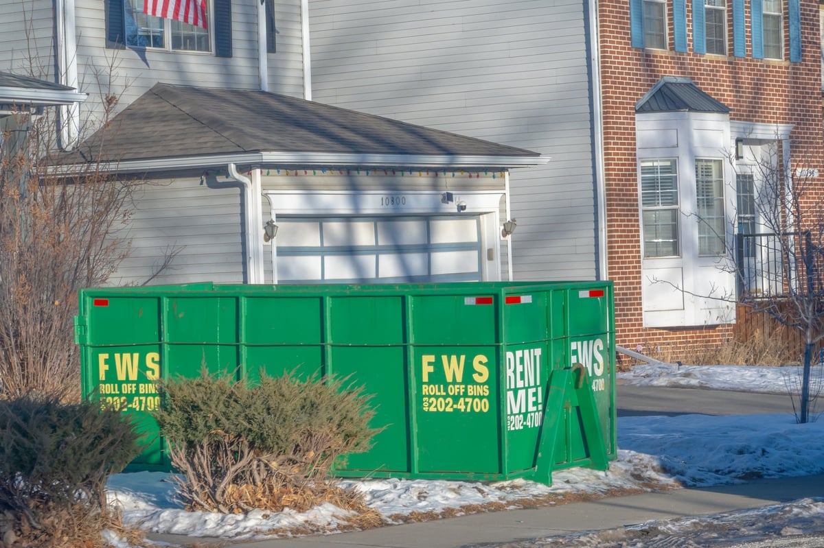 A large roll-off waste bin sits on a residential driveway