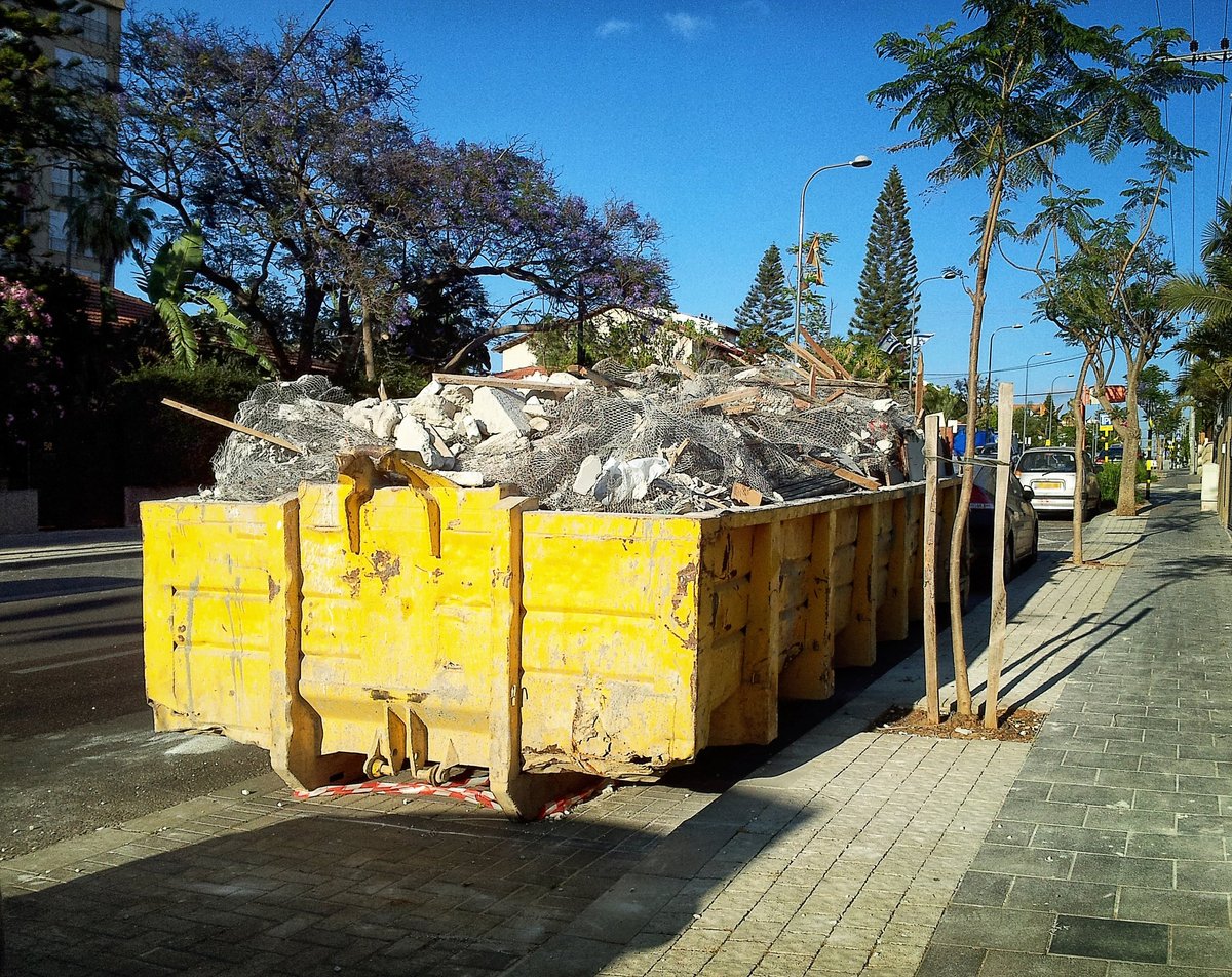 Yellow roll-off container parked on the street filled with construction trash