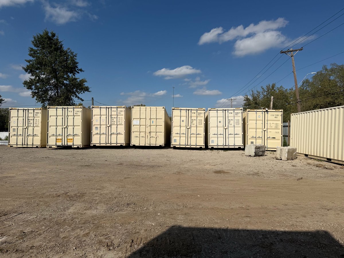 Row of cream-colored shipping containers in an outdoor storage yard under blue sky