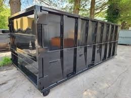 Black metal livestock trailer or storage container with barred windows on a concrete surface surrounded by trees