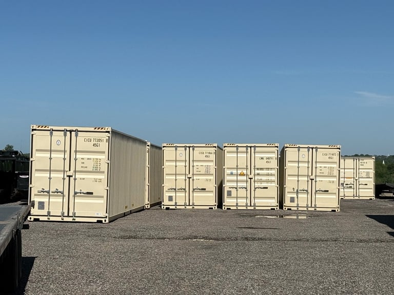 Row of tan and white shipping containers lined up on a paved lot under clear blue sky