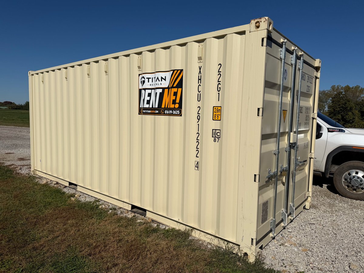 Beige shipping container with Titan Rent logo and identification numbers on its side, parked outdoors near a white truck